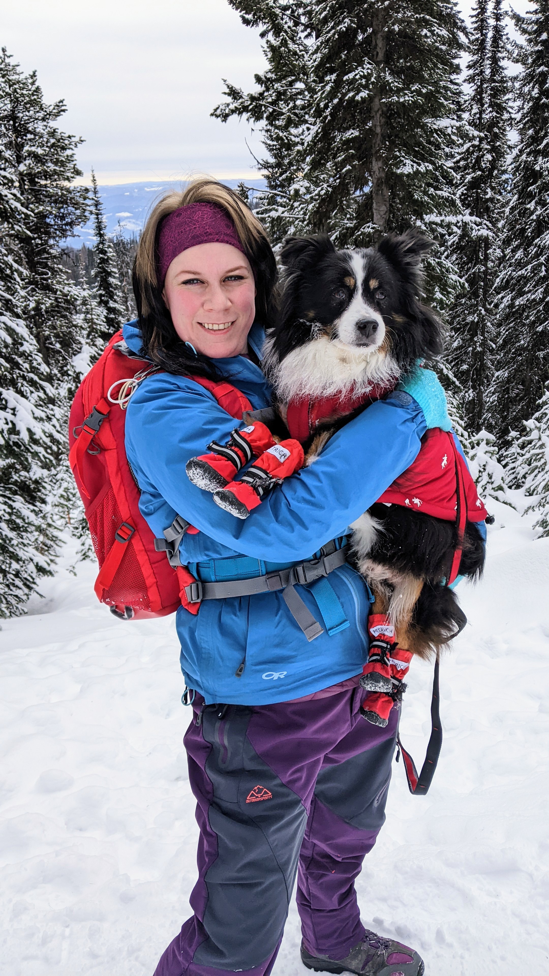 Girl holds her dog in front of snow covered trees and mountains