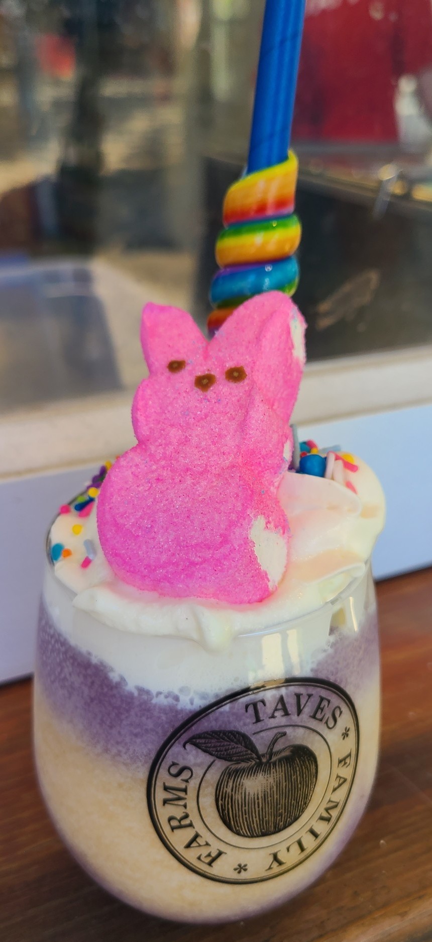 A purple and golden slushie in a Taves Farm cup with whipped cream, a pink marshmellow peep, and candy straw.